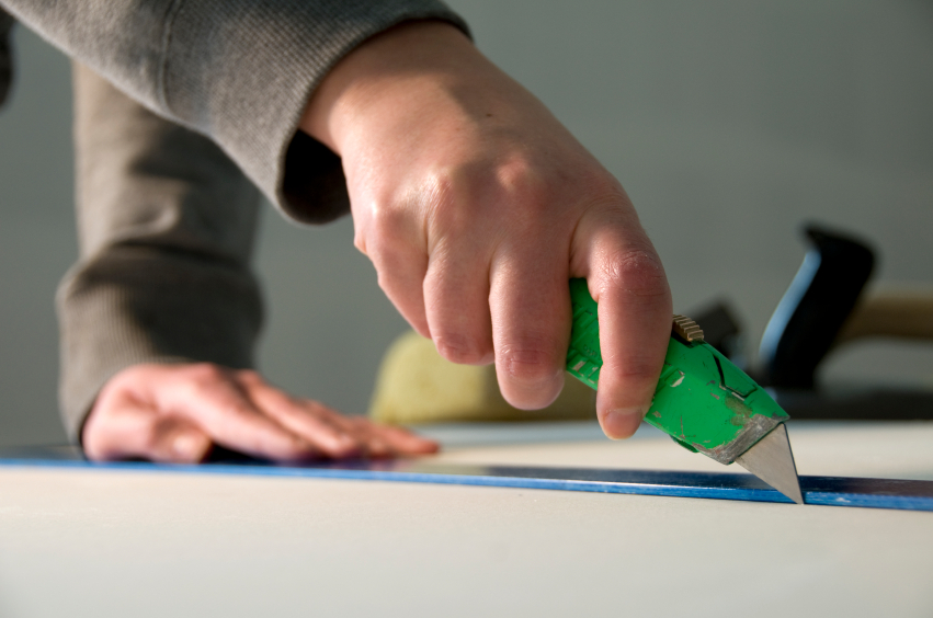 A worker cuts drywall with a knife. 