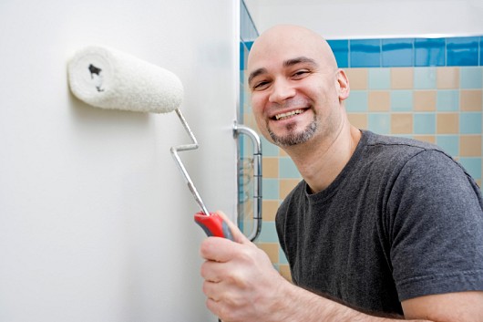 Photo of a DIY-er painting a bathroom wall by michellegibson/istockphoto.com.